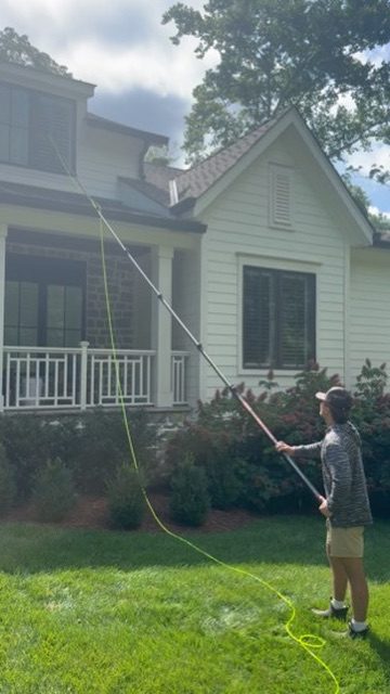 Technician cleaning upper-story windows from the lawn with a long water-fed pole